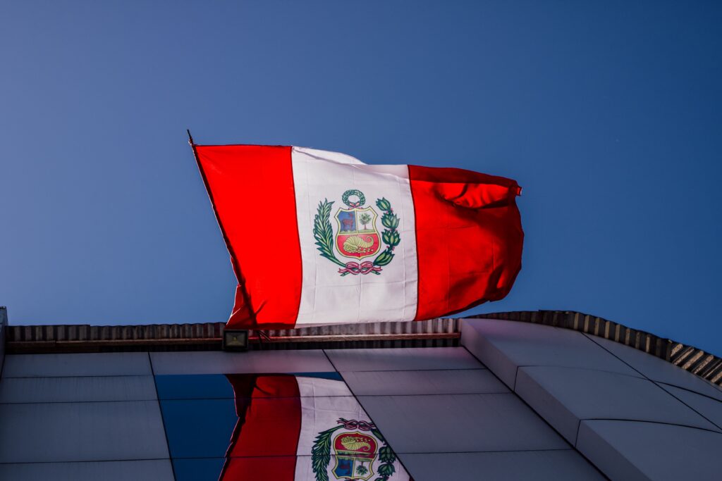 National Peruvian flag waving prominently against a clear blue sky, reflecting on a building.